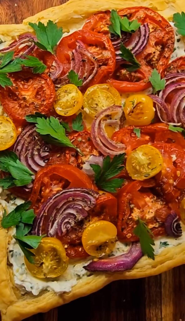 Roasted tomato tart with flaky puff pastry, creamy herb cheese spread, sliced tomatoes, red onion, and fresh parsley