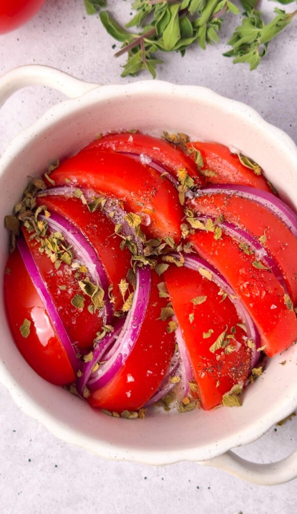 Tomatoes and red onion seasoned with olive oil, oregano, salt, and pepper before roasting