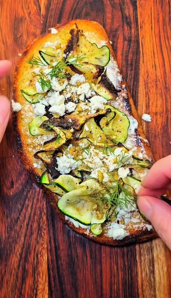 Finished zucchini toast with feta, dill, and olive oil, served warm on toasted sourdough