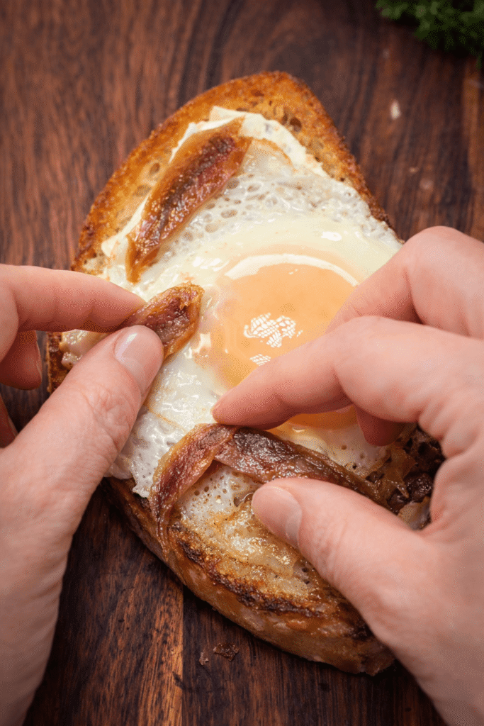 Adding anchovies to fried egg on toast for rich umami flavor in savory breakfast toast recipe