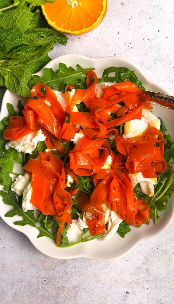 Roasted carrot ribbons layered over burrata and arugula to make roasted carrot burrata salad