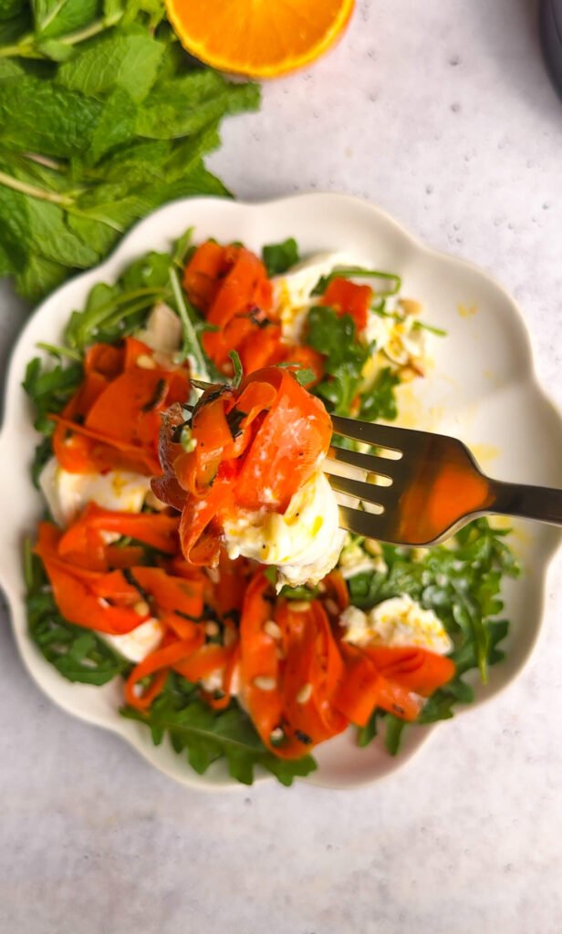 Fork lifting burrata with roasted carrot ribbons and arugula from roasted carrot burrata salad