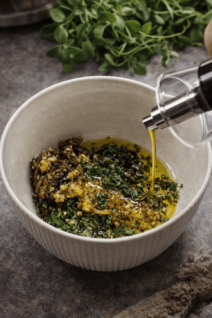 Homemade herb chili oil with garlic, fresh herbs, and olive oil being mixed in a bowl