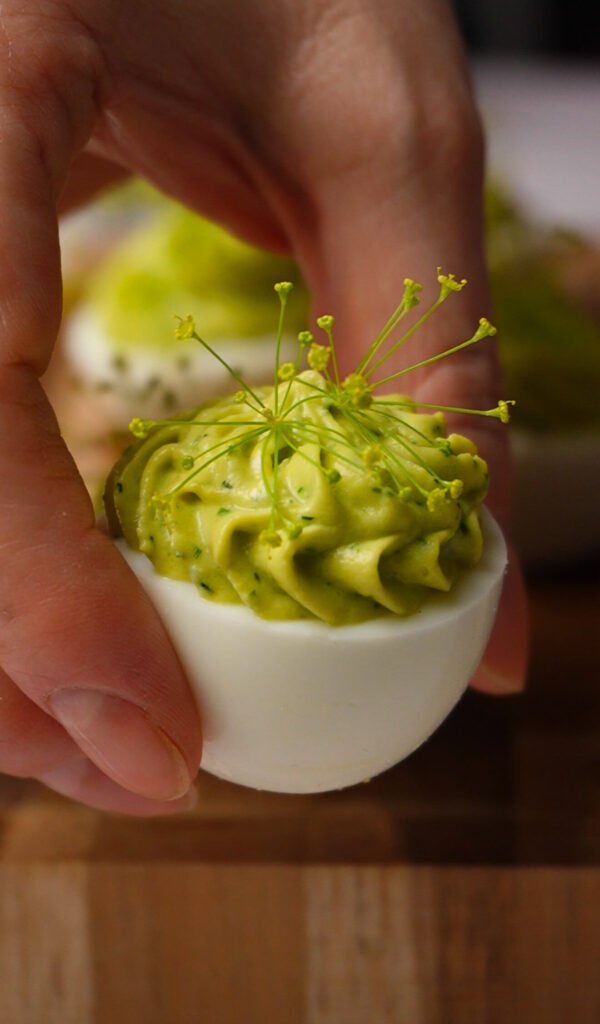 hand holding green goddess deviled egg with creamy avocado herb filling and dill flower garnish