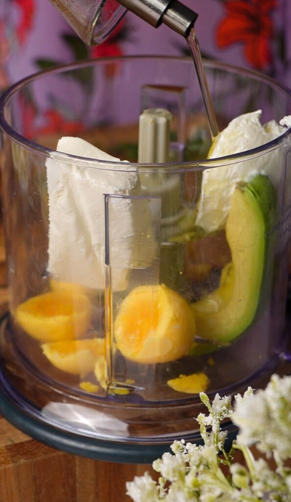ingredients for green goddess deviled eggs in food processor with egg yolks avocado cream cheese and olive oil
