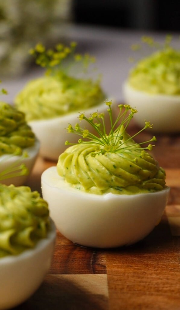 platter of green goddess deviled eggs with smooth avocado filling and fresh herb garnish