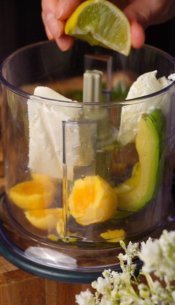 adding fresh lemon juice to green goddess deviled egg filling with avocado and herbs in food processor