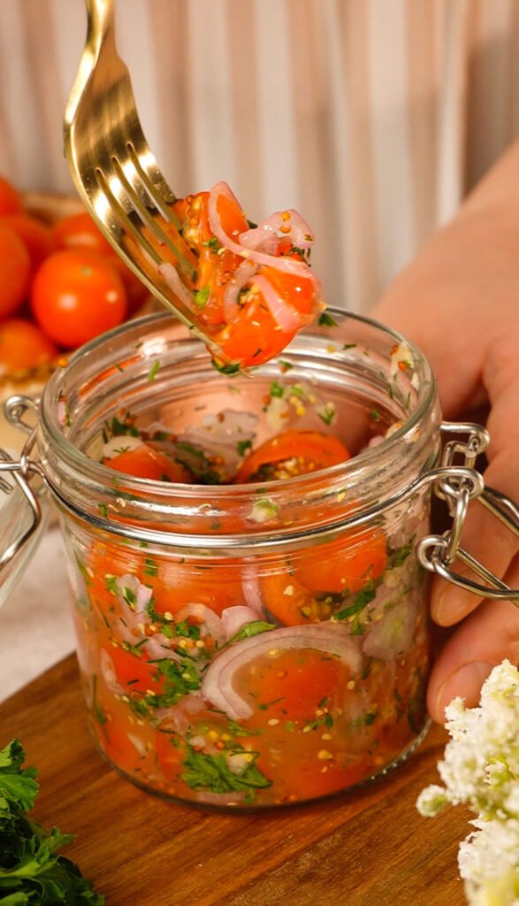 quick marinated cherry tomatoes with garlic herbs and red onion in glass jar close up
