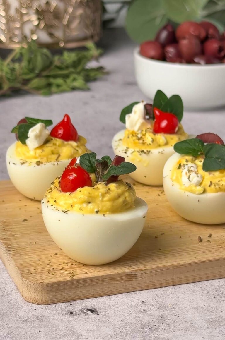 Mediterranean deviled eggs garnished with olives feta oregano and pepper drops on wooden board