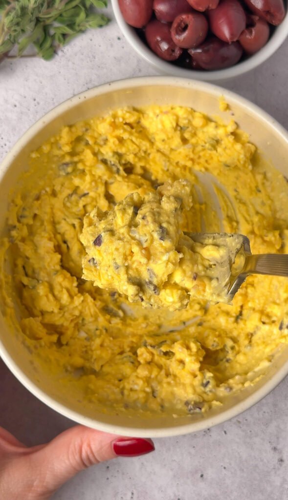 Creamy Mediterranean deviled egg filling with feta olives and capers in mixing bowl