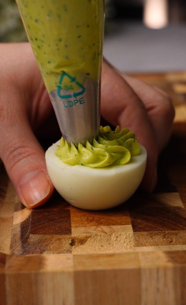 piping creamy avocado herb filling into egg whites for green goddess deviled eggs using star tip