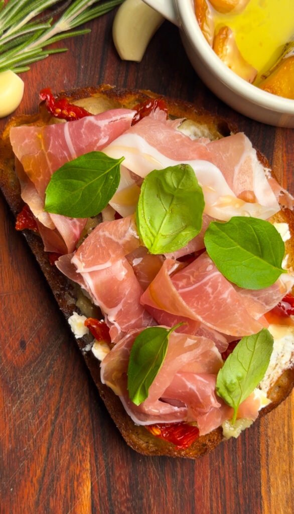 Prosciutto goat cheese toast with sun-dried tomatoes and basil on toasted sourdough bread