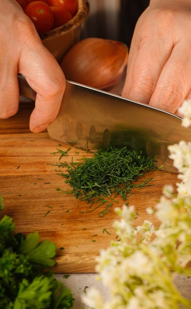 chopping fresh dill for marinated cherry tomatoes recipe on wooden cutting board