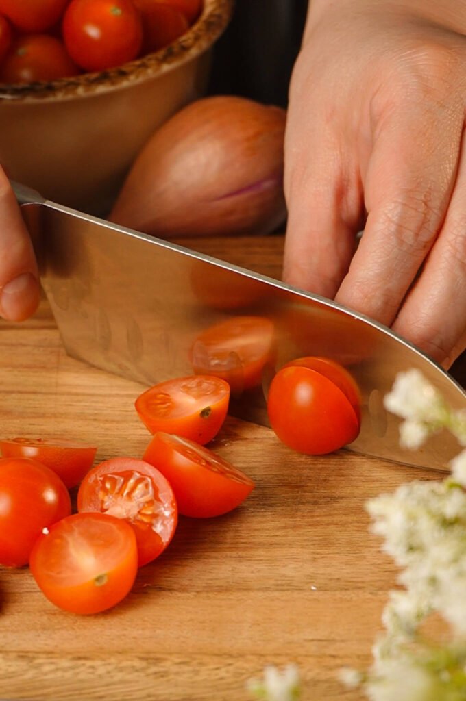 halving cherry tomatoes for marinated tomato recipe on cutting board