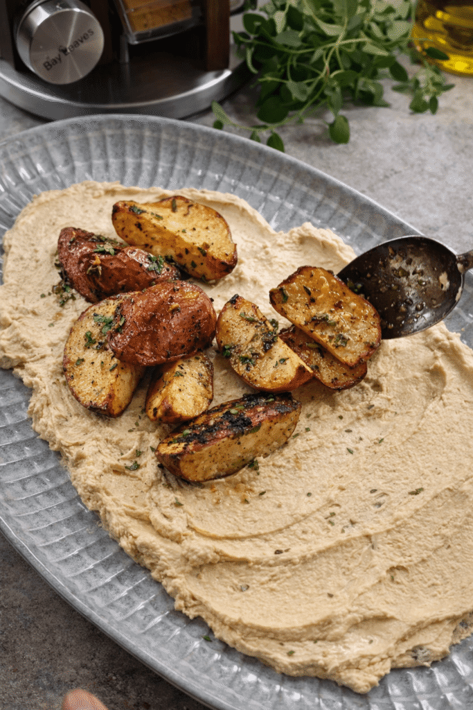 Crispy roasted potatoes being placed over creamy whipped feta sauce on a serving plate