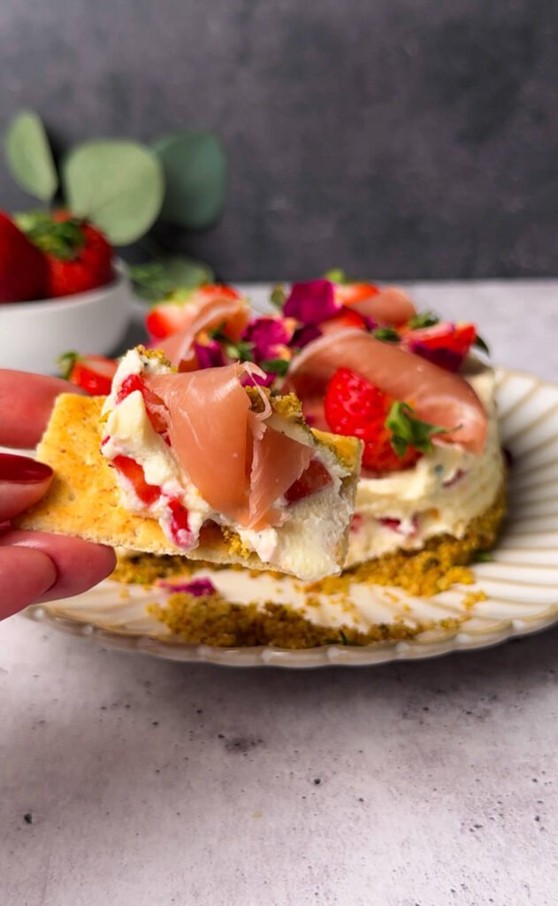 Cracker topped with strawberry prosciutto cheesecake dip showing creamy ricotta filling, fresh strawberries, and prosciutto in a sweet savory appetizer bite.