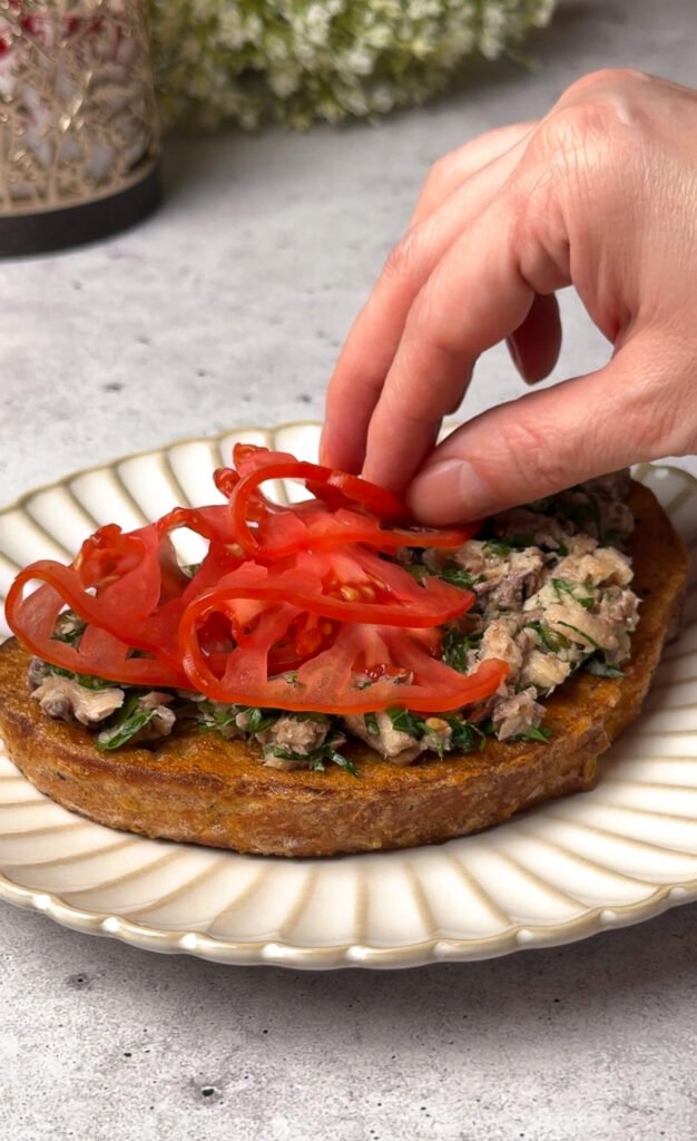 layering thin heirloom tomato slices over sardine toast
