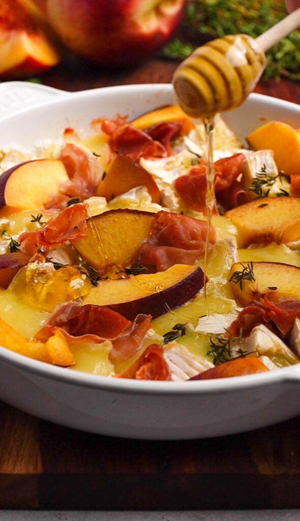 Drizzling hot honey over baked brie with peach and prosciutto fresh out of the oven