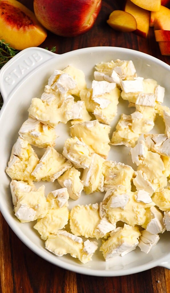 Chunks of brie arranged in a baking dish for baked brie with peach and honey appetizer