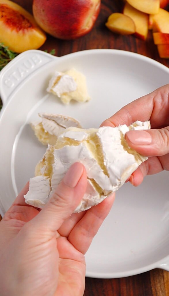 Tearing a wheel of brie into pieces for baked brie with peach and hot honey in a white baking dish