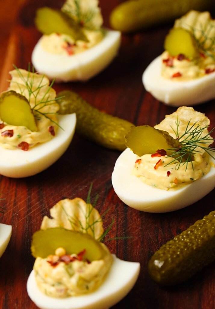 dill pickle deviled eggs arranged on board with crispy toppings and fresh herbs