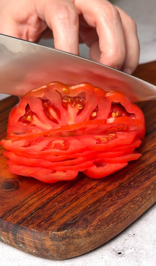 thinly slicing ripe heirloom tomato on wooden board for tomato toast
