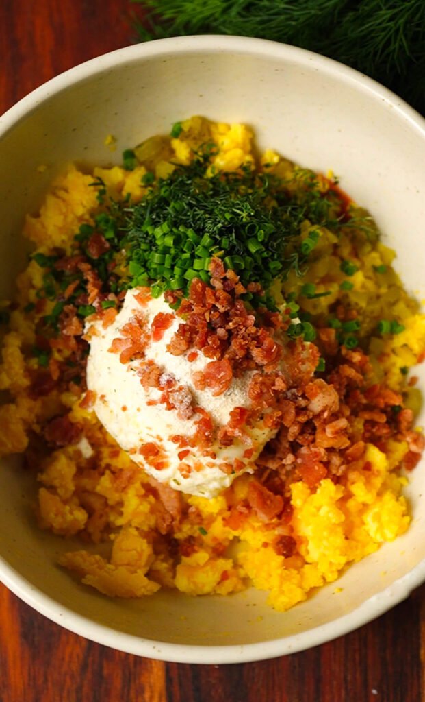 deviled egg yolk mixture with cream cheese bacon dill pickles and chives before mixing