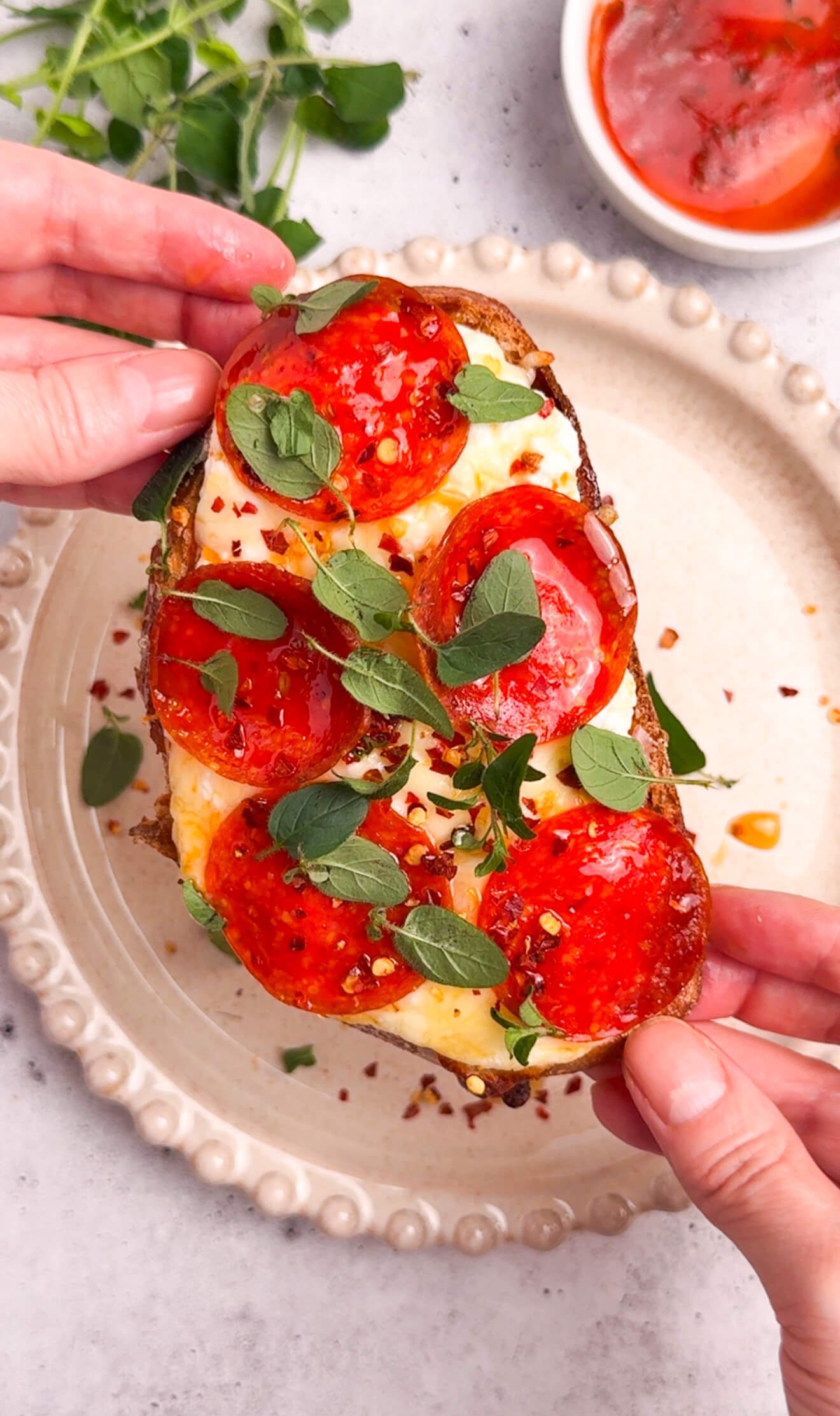 hand holding pizza toast with melted cheese pepperoni and herbs close up