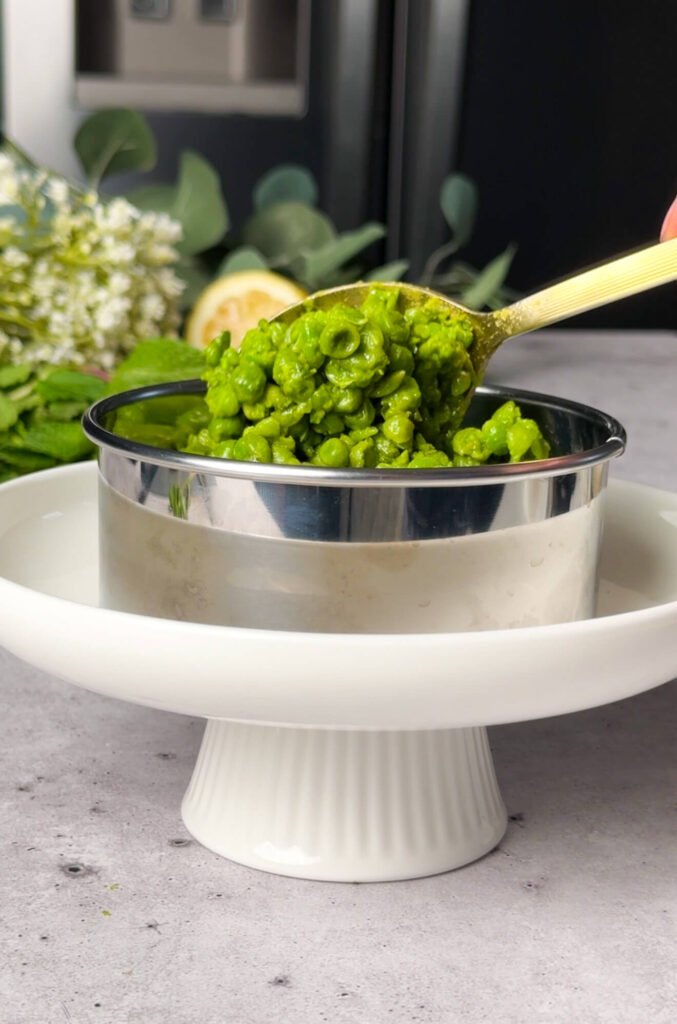 spooning mashed peas into ring mold for layering ricotta pea timbale appetizer