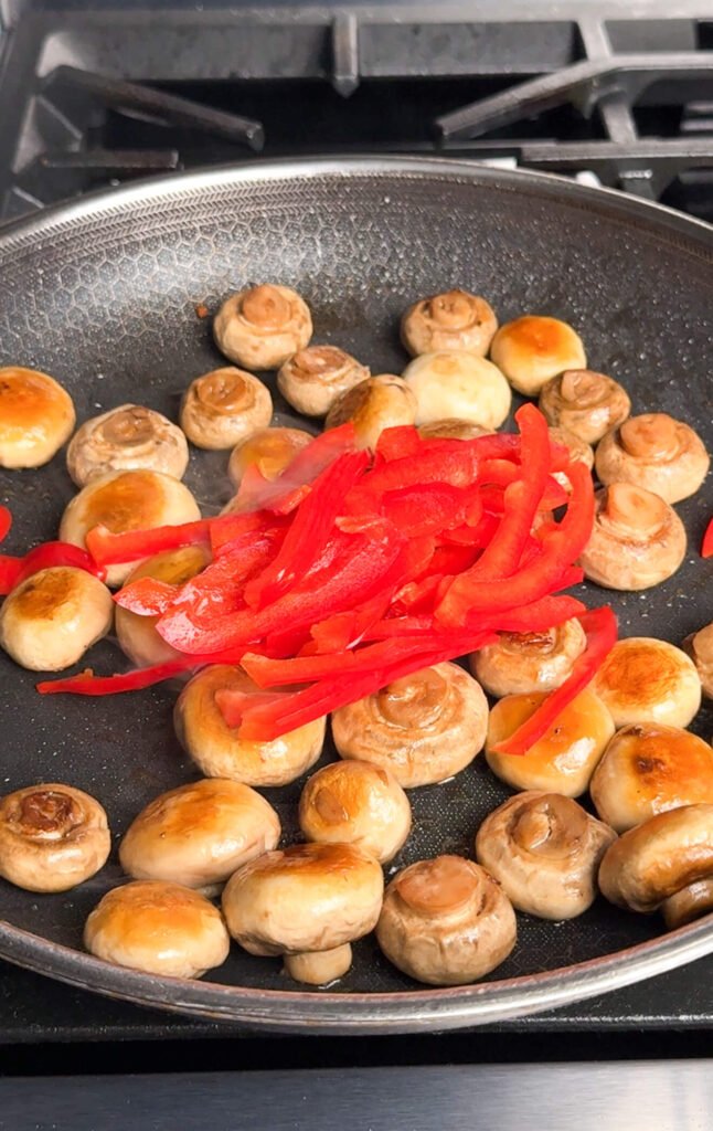 sautéing mushrooms and red bell peppers in skillet for marinated mushroom recipe