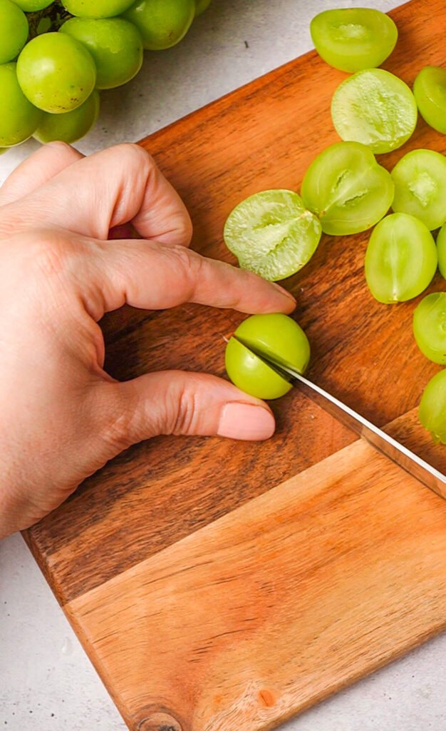 slicing green grapes on cutting board for fresh waldorf salad with burrata