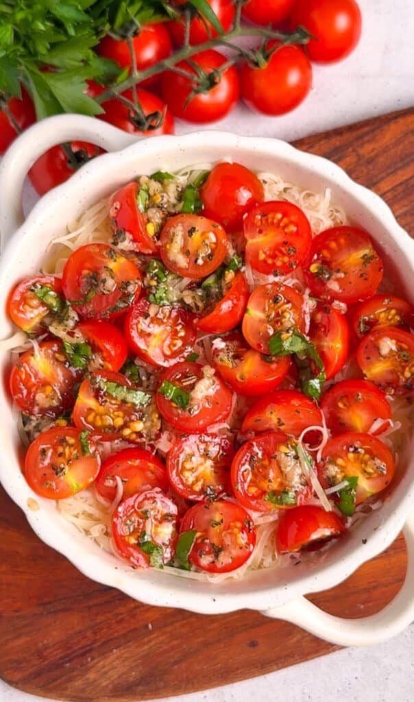 Seasoned cherry tomatoes layered over shredded cheese in a scalloped white baking dish, ready to go into the oven