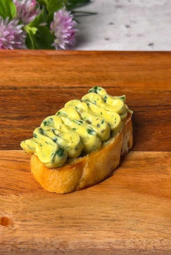 Whipped egg and herb spread piped in a swirl onto a toasted baguette slice on a wooden board