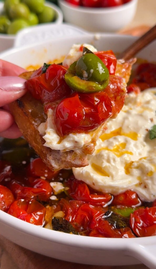 burrata toast topped with roasted tomatoes and olives on crispy bread