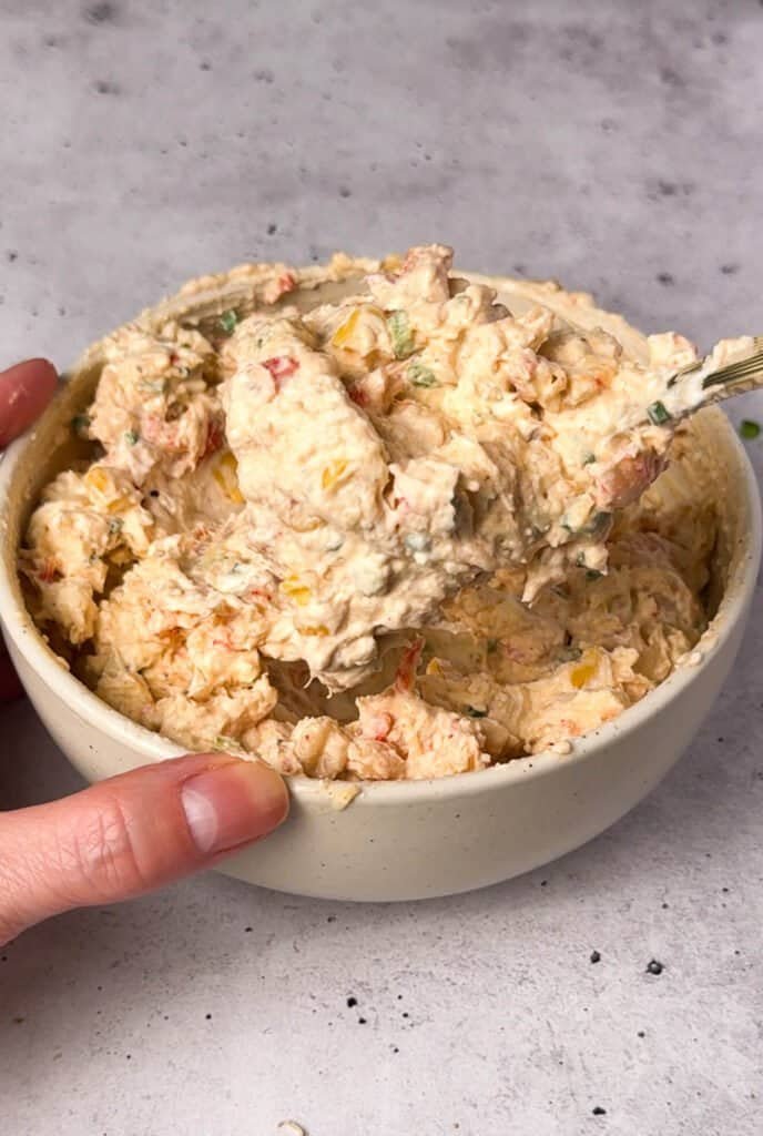 Cajun crawfish cream cheese filling with visible crawfish, roasted corn, and jalapeño being scooped from a ceramic bowl with a gold spoon