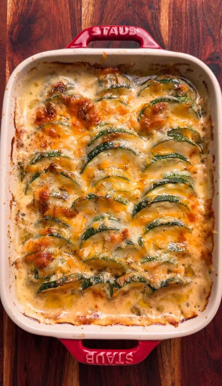 Overhead view of cheesy zucchini casserole with melted Swiss and cheddar cheese in a red Staub baking dish