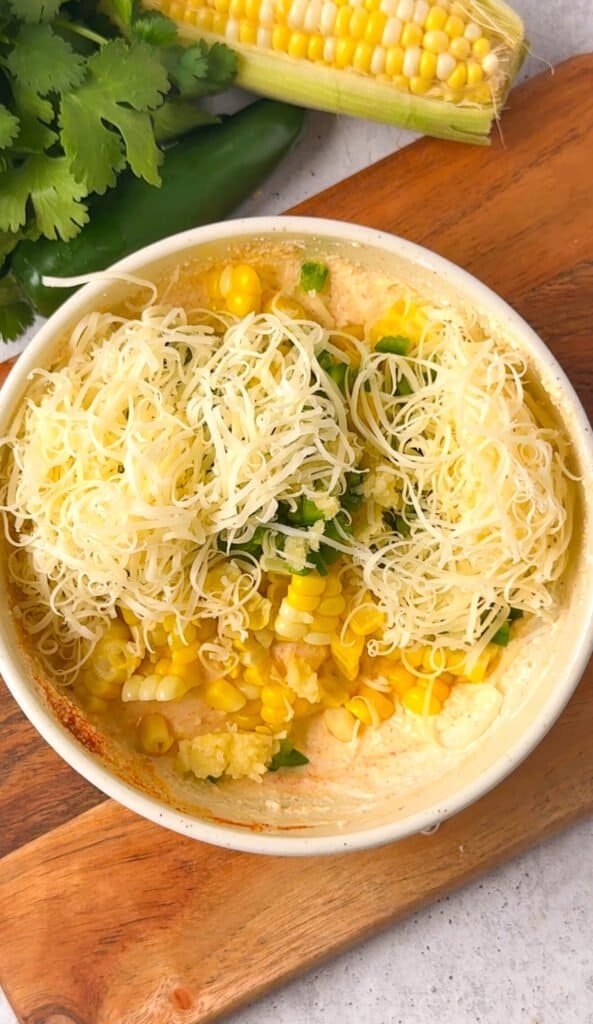 Corn and jalapeño dip mixture in a white ceramic dish showing fresh corn kernels and shredded pepper jack cheese before baking