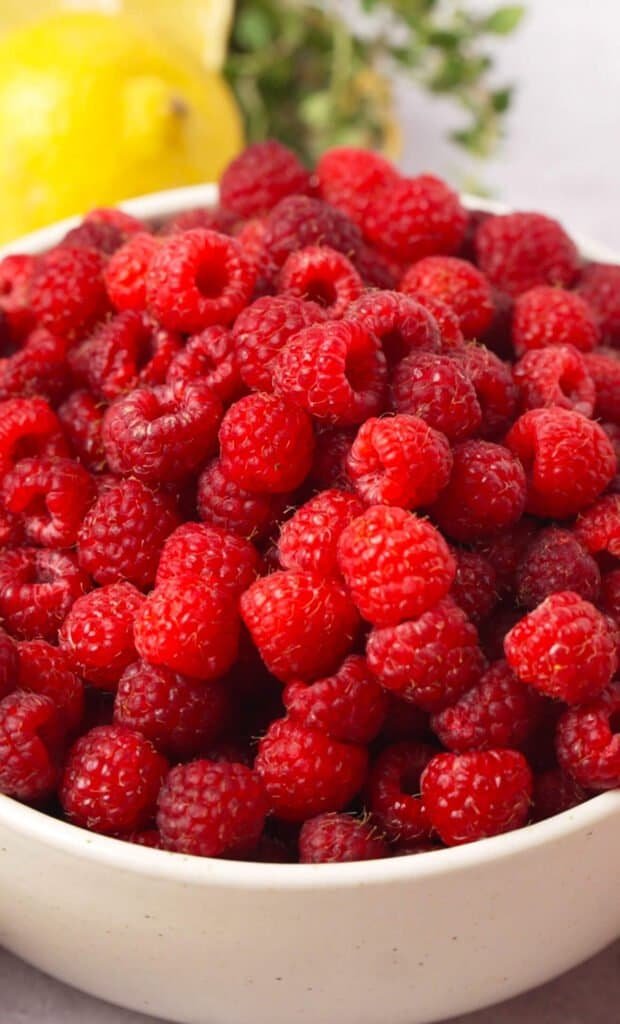 Close up of fresh raspberries in a bowl with lemon and thyme in the background
