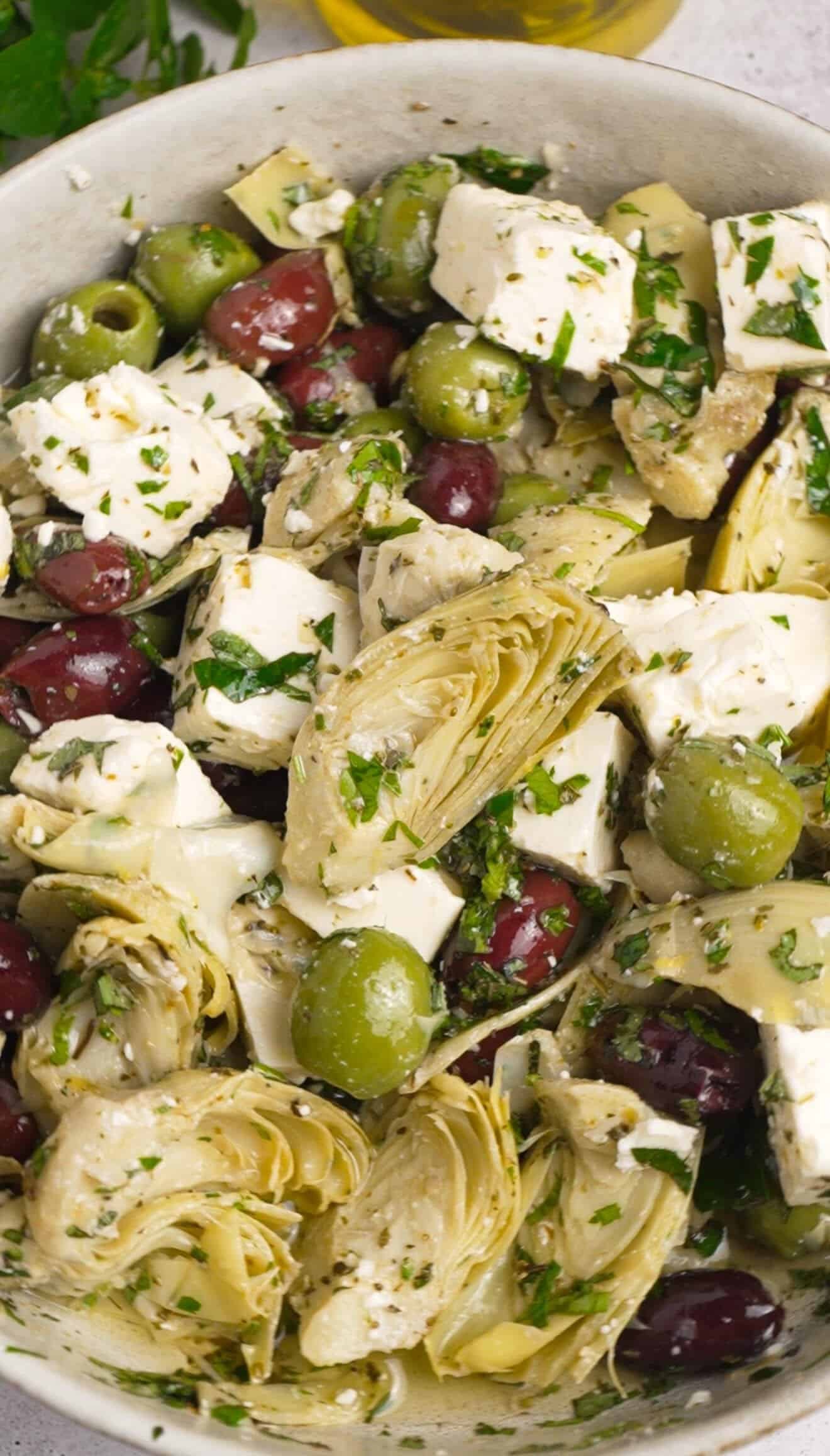 Overhead close-up of marinated feta with artichoke hearts, Castelvetrano and Kalamata olives in a garlicky herb marinade