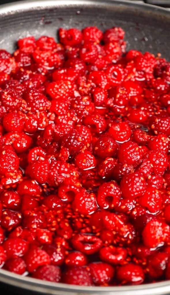 Raspberries simmering in a saucepan while cooking down into preserve