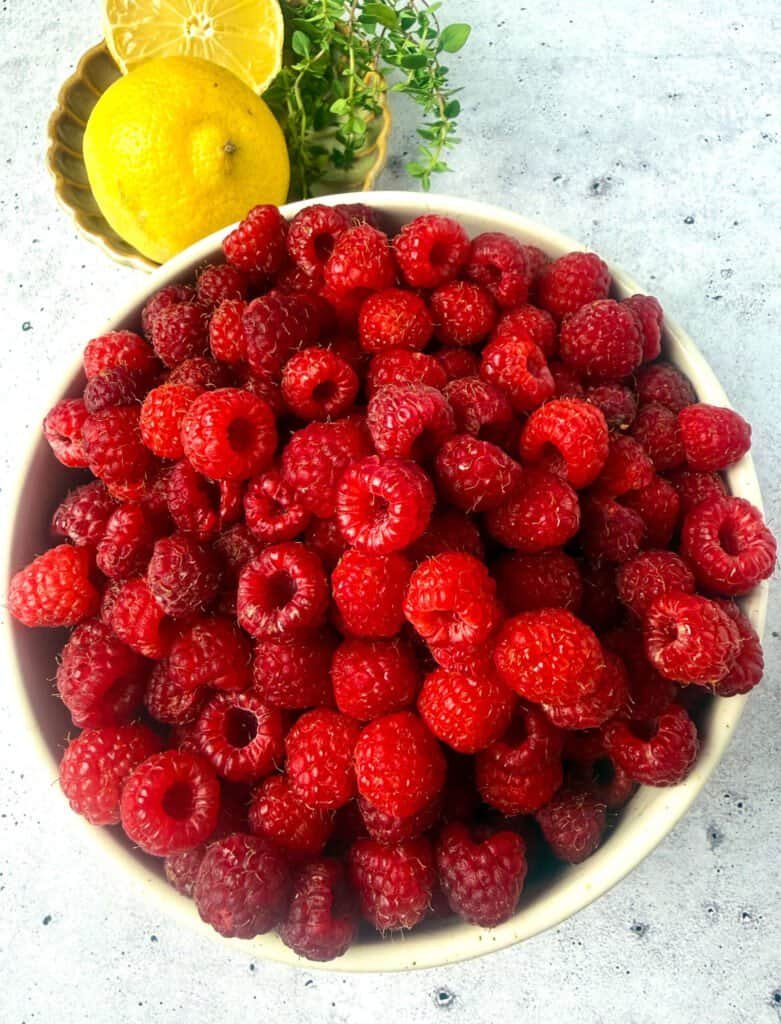 Overhead view of fresh raspberries in a bowl with lemon and thyme for raspberry vanilla preserve
