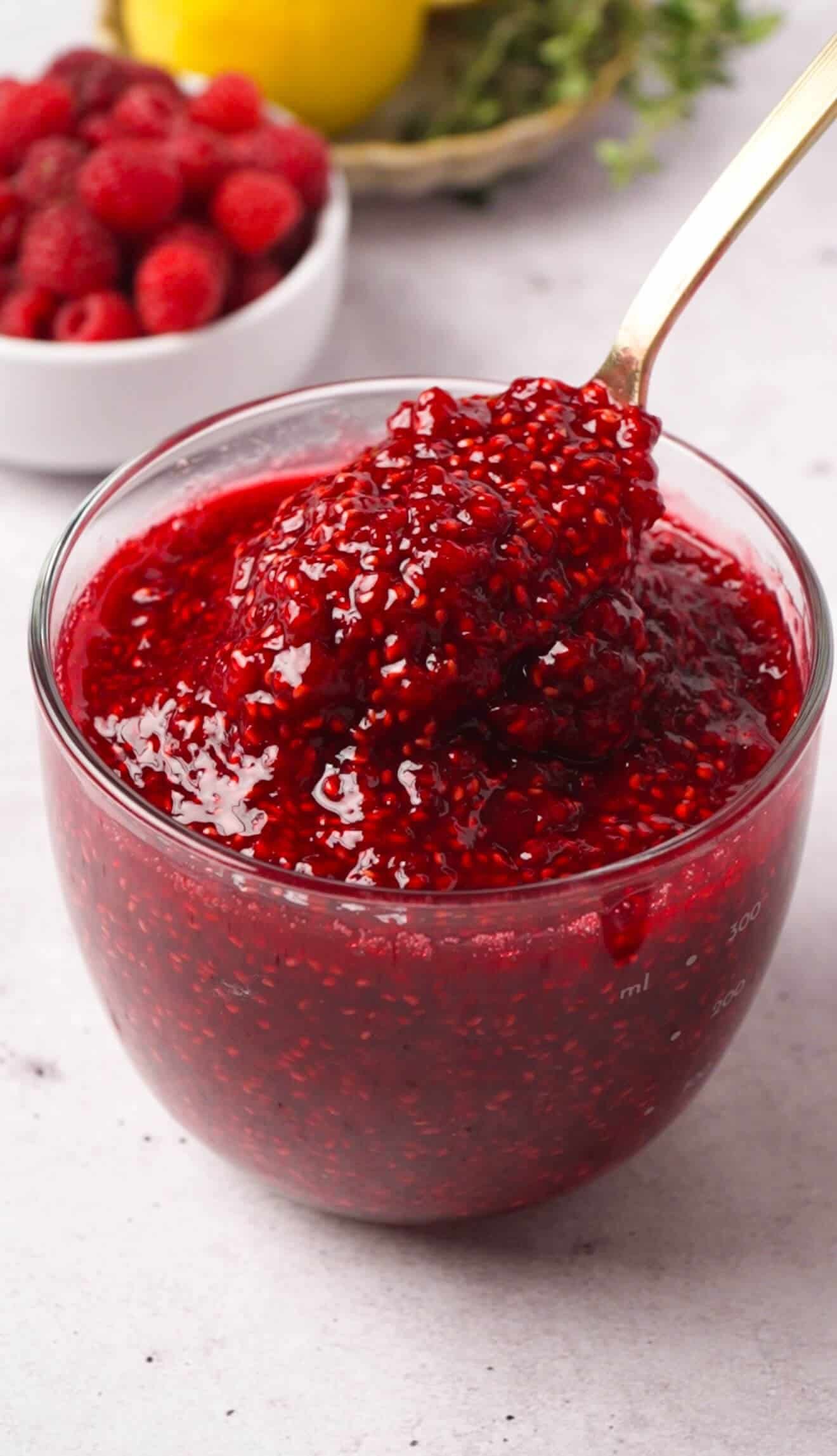 Spoon lifting a scoop of finished raspberry vanilla preserve from a glass jar