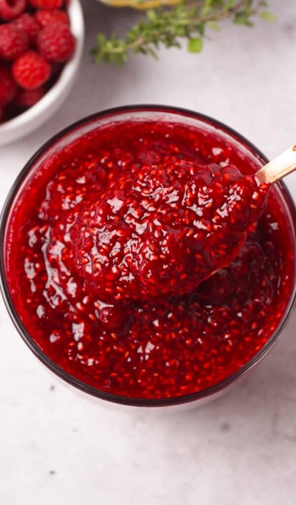 Overhead close up of glossy raspberry vanilla preserve with a spoon in a glass jar