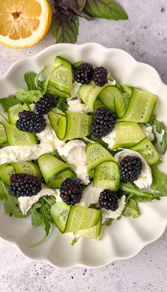 Blackberry burrata salad with cucumber ribbons and torn burrata on a scalloped white platter