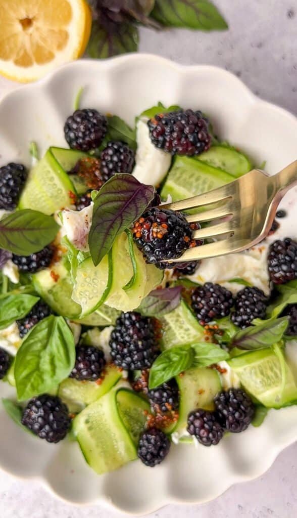 Close-up of blackberry burrata salad with honey Dijon dressing and a fork lifting a blackberry