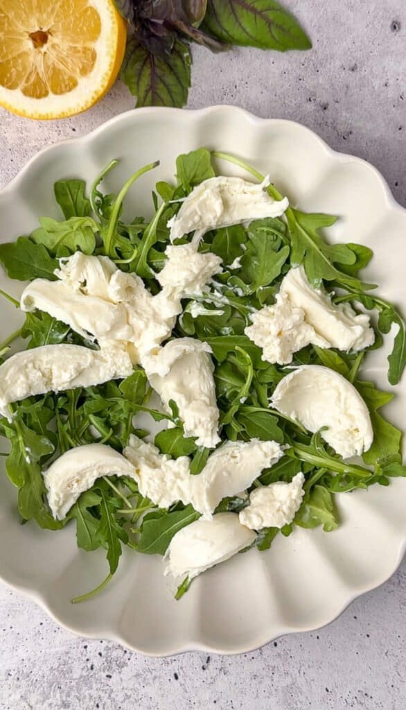 Fresh burrata torn over a bed of baby arugula before assembling blackberry salad