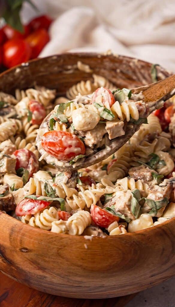 Close-up of creamy balsamic chicken pasta salad coated in dressing with fresh basil and cherry tomatoes