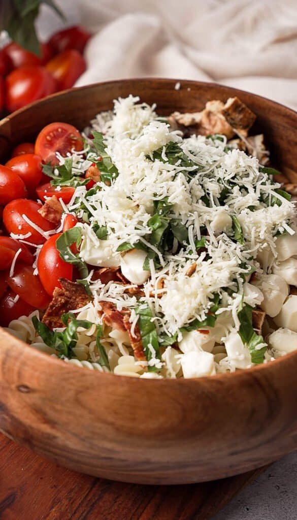 Creamy balsamic chicken pasta salad topped with shredded parmesan and fresh basil before tossing