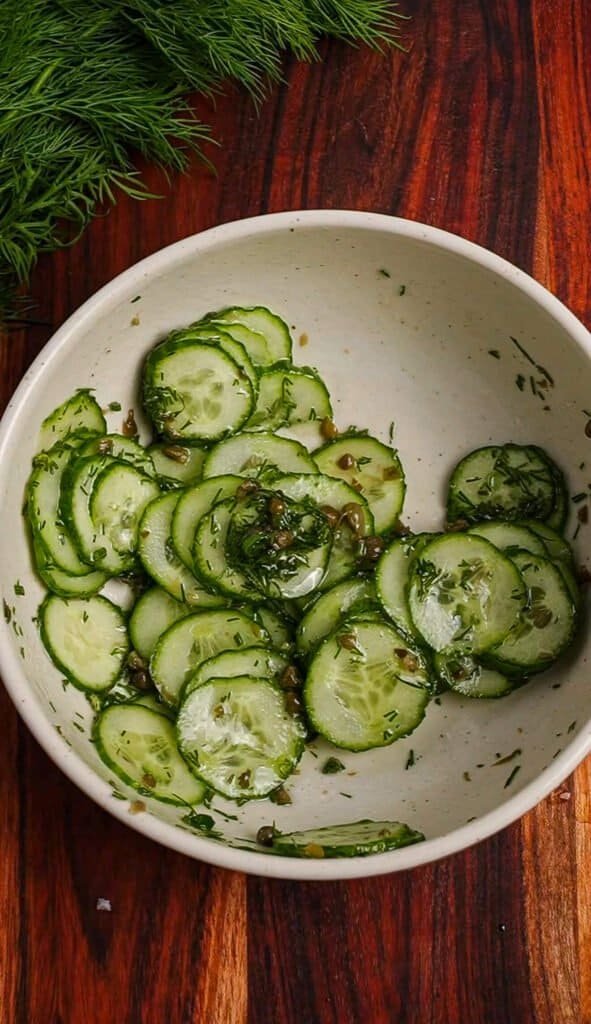 Cucumber caper salad tossed with champagne vinegar, fresh dill, and capers in a white ceramic bowl