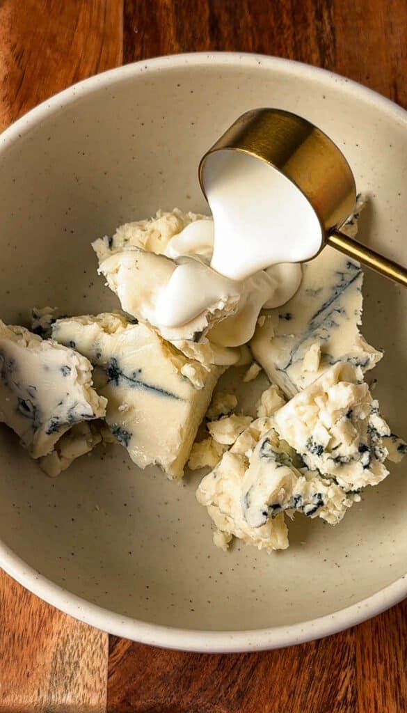 Chunks of gorgonzola cheese in a bowl with whipped cream being poured over top